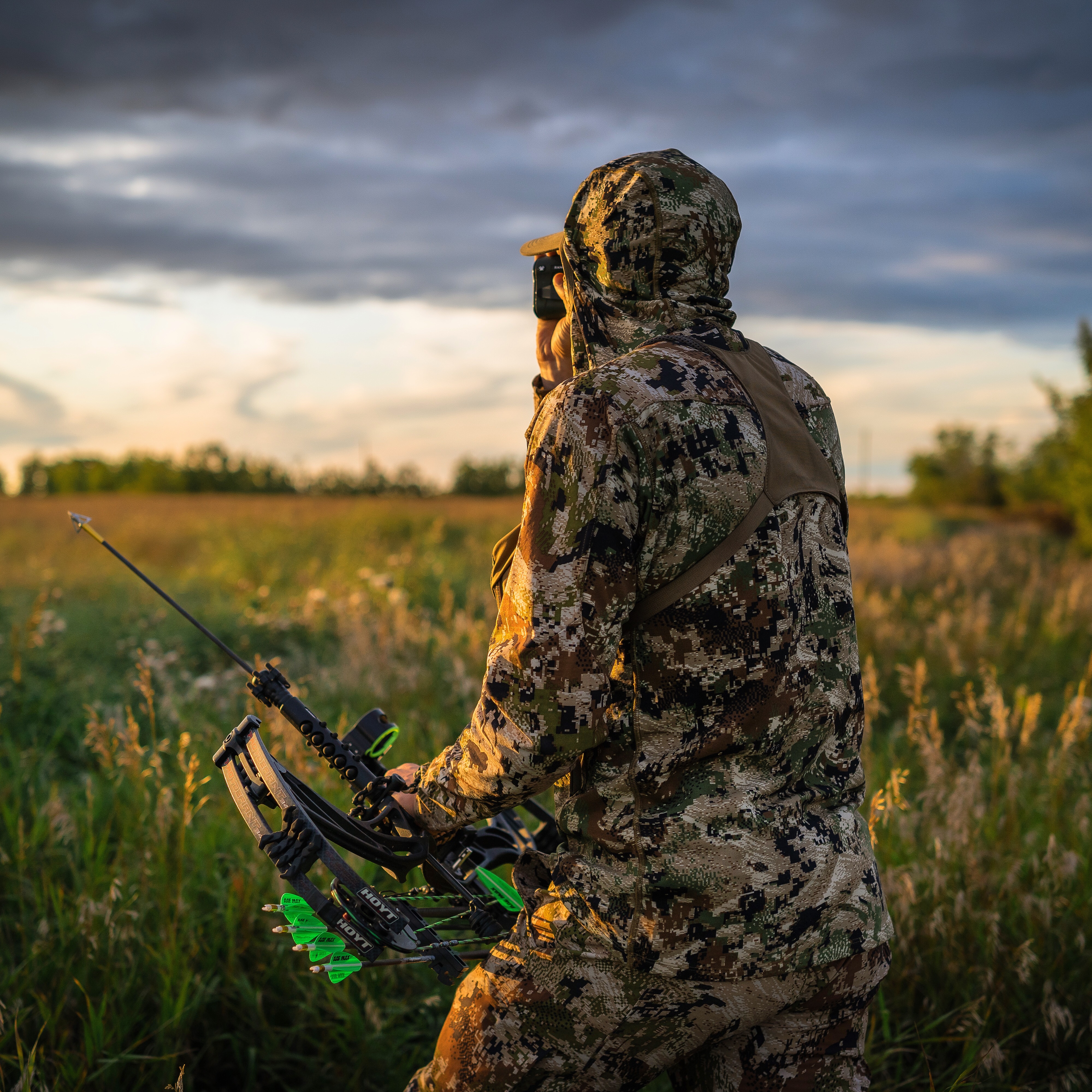 a bowhunter is ranging his target during last light on the boundary of a hay field